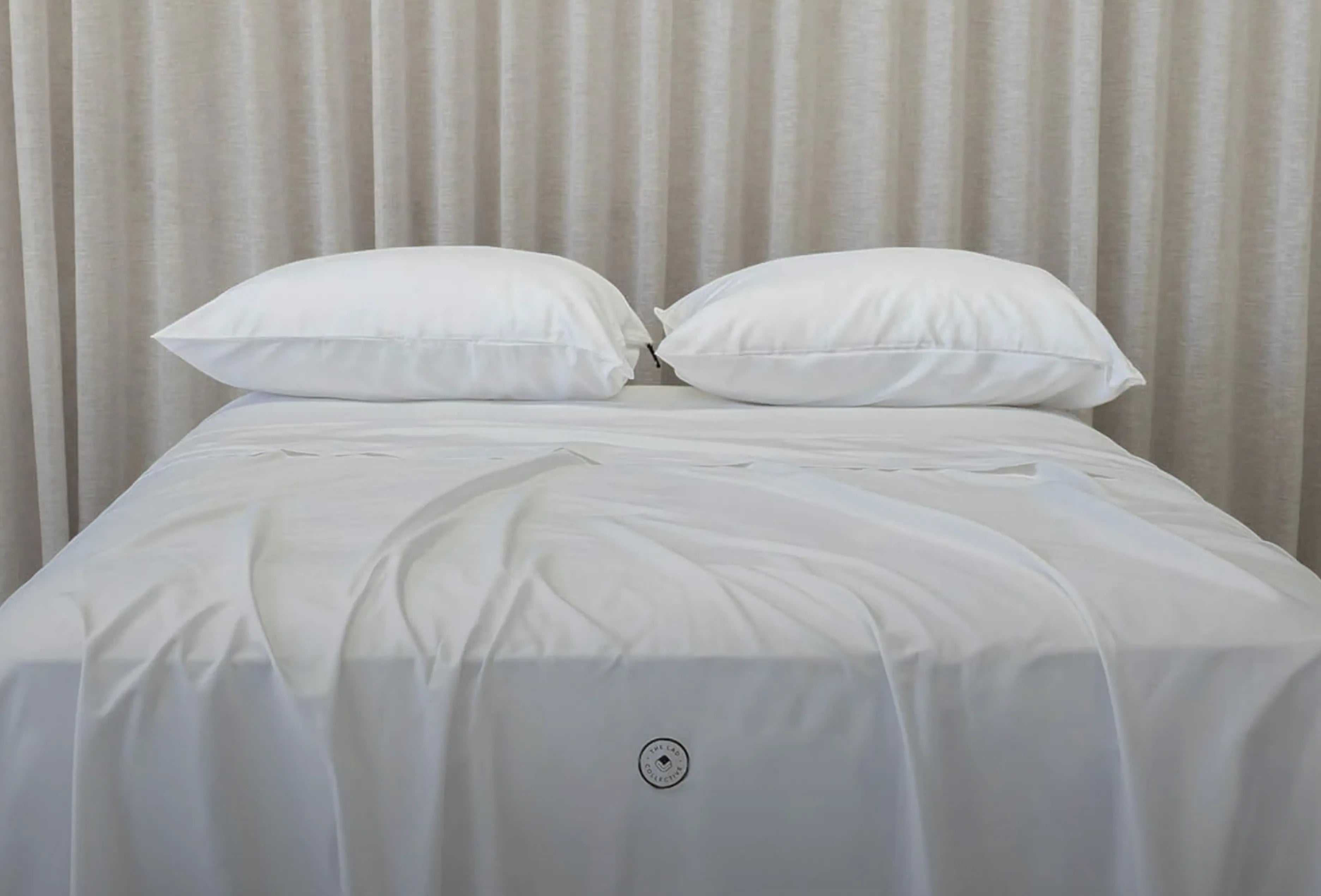 White bed with two pillows against a neutral curtain background