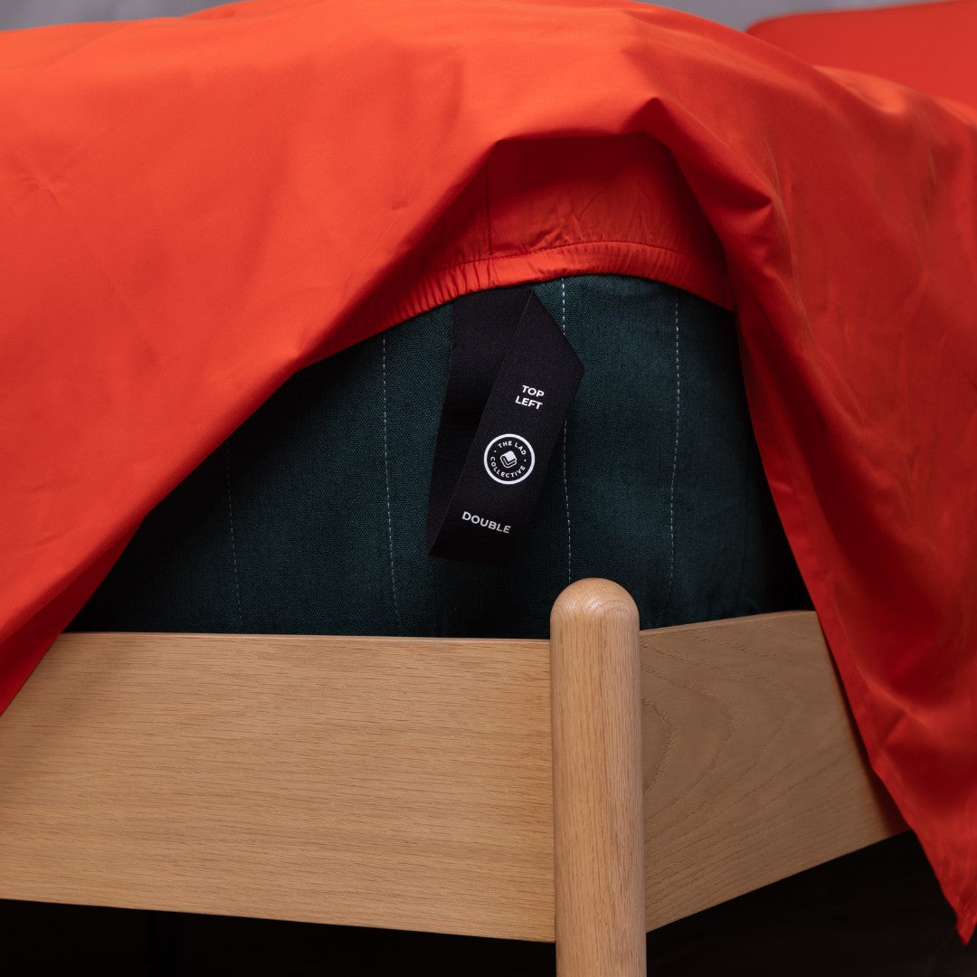 Close-up of labeled JoeyPouch™️ corner strap on TLC Red Rock fitted sheet over mattress.