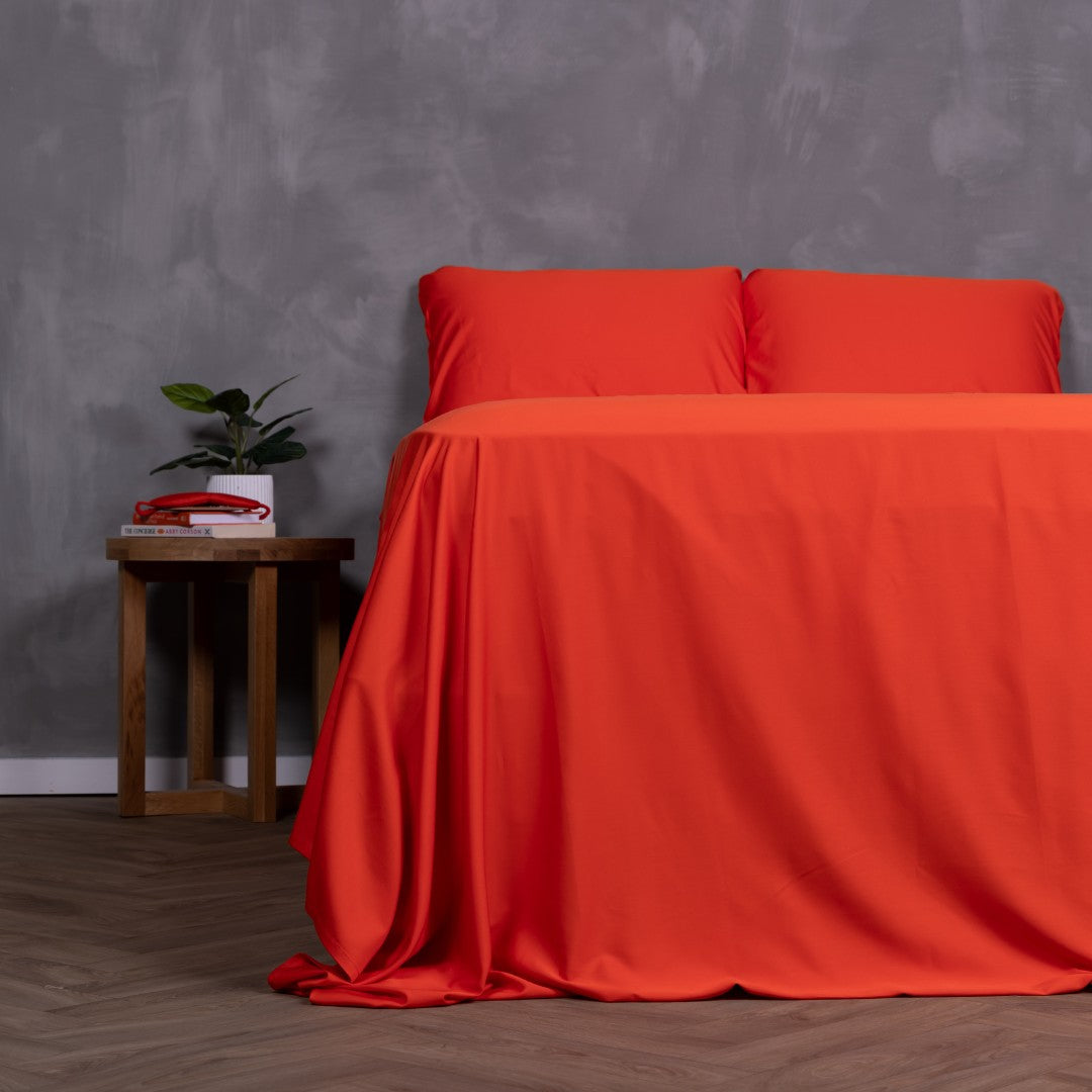 Red Rock bedding set draped over bed with two pillows, styled with bedside table and house plant.