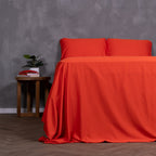 Red Rock bedding set draped over bed with two pillows, styled with bedside table and house plant.