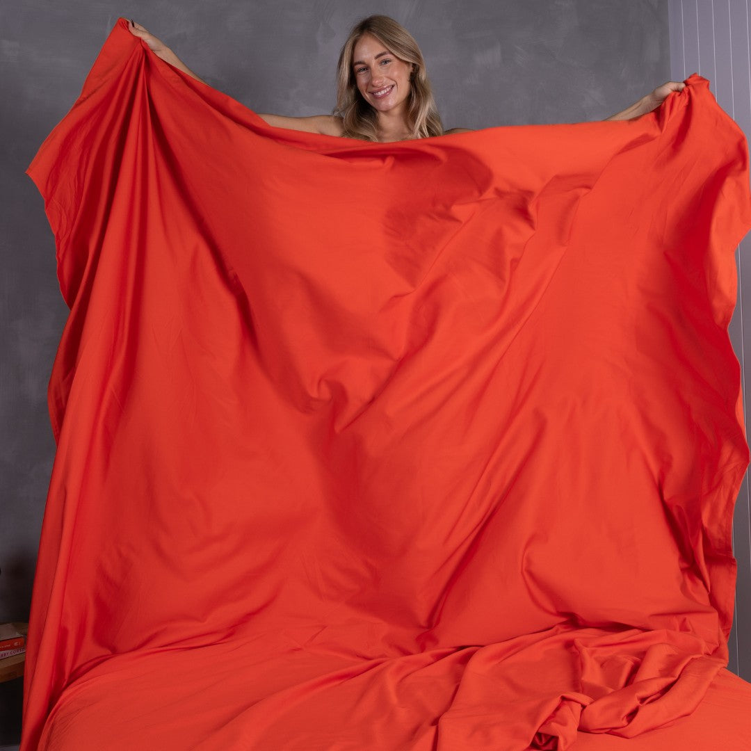 Woman smiling while holding up oversized TLC Red Rock top sheet in front of grey wall.