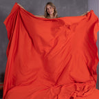 Woman smiling while holding up oversized TLC Red Rock top sheet in front of grey wall.