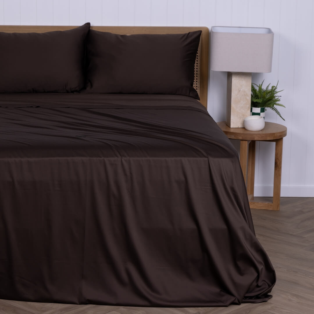 Brown bed sheets on a bed with a wooden nightstand and lamp in the background.