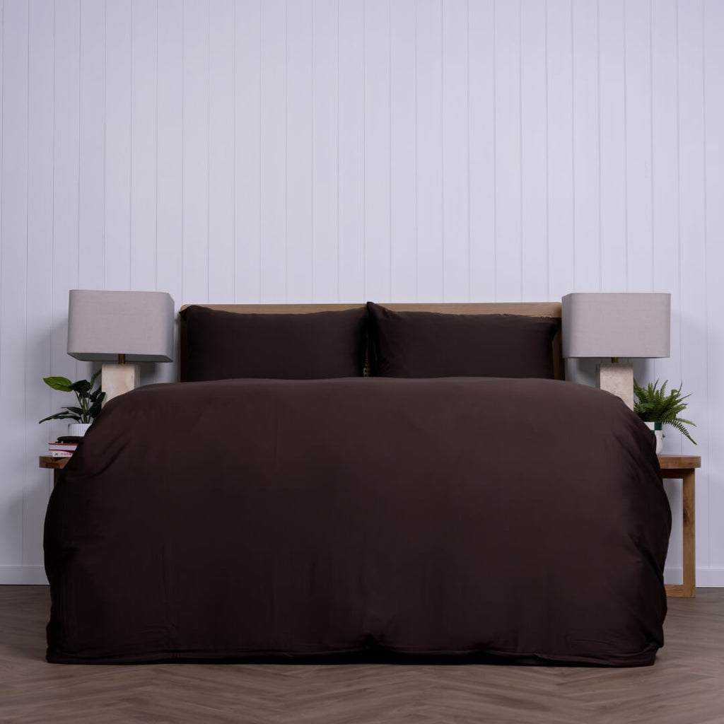 Brown bedspread set on a bed with matching pillows against a white pannel wall.