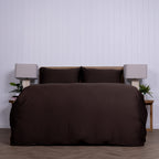 Brown bedspread set on a bed with matching pillows against a white pannel wall.