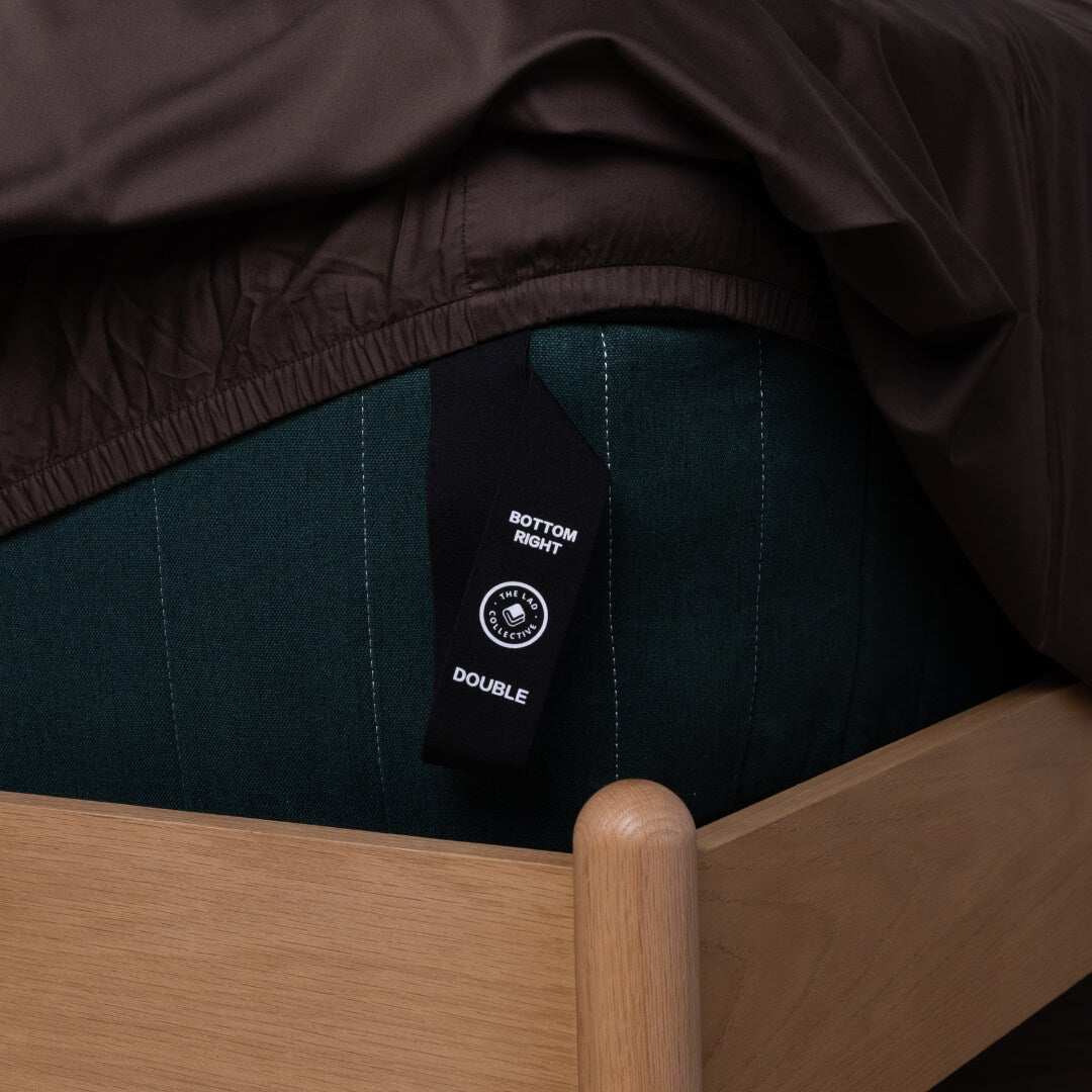 Dark brown fitted sheet with a labeled loop corner strap hanging off the bed.