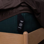 Dark brown fitted sheet with a labeled loop corner strap hanging off the bed.